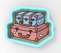 A cookie cutter-shaped illustration depicting two suitcases, one blue and one pink, stacked on top of each other.