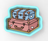 A cookie cutter-shaped illustration depicting two suitcases, one blue and one pink, stacked on top of each other.