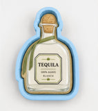 A blue cookie cutter shaped like a bottle of tequila, with a label that reads "100% AGVEC BLANCO".