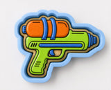 A cookie cutter shaped like a water gun, with a vibrant green handle and an orange barrel.