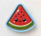 A cookie shaped like a slice of watermelon with a smiling face and black dots on top.