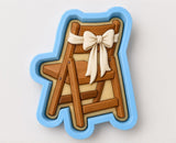 A cookie cutter in the shape of a wooden chair with a white bow on it.