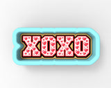 A blue cookie cutter with the word "XOXO" printed on it, surrounded by red heart shapes.